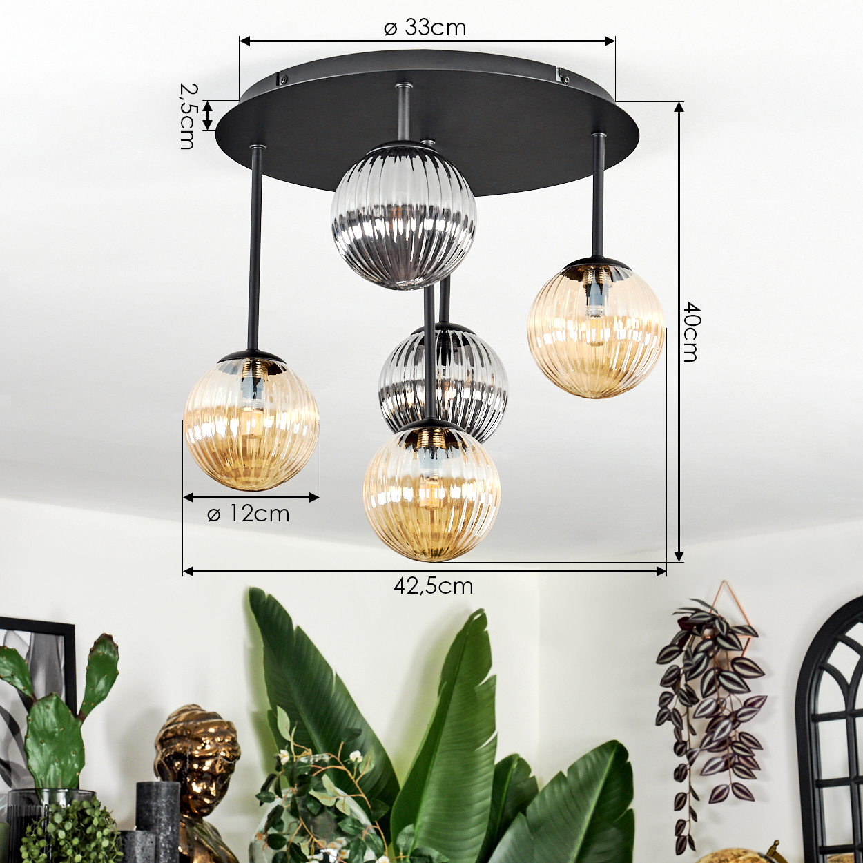 Eine moderne Deckenlampe mit vier Glasschirmen in Bernstein und Silber, die von einer schwarzen runden Basis hängen. Pflanzen und Deko im Hintergrund.