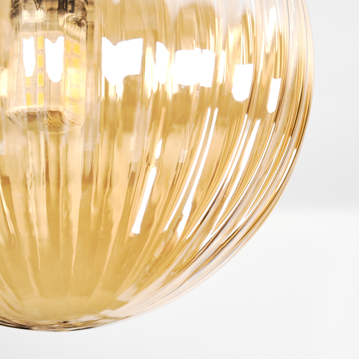 Nahaufnahme eines goldenen Glaslampenschirms mit vertikalen Rippen. Eine beleuchtete Glühbirne ist oben zu sehen, vor weißem Hintergrund.