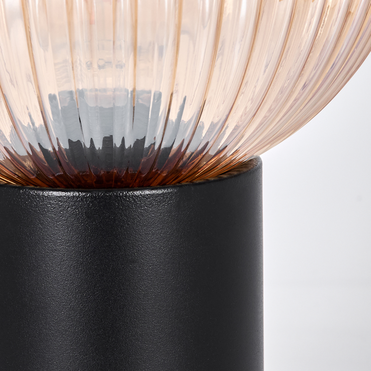 Nahaufnahme einer Lampe. Sie hat einen runden, gerippten, orange getönten Glaskopf und einen schwarzen zylindrischen Sockel.