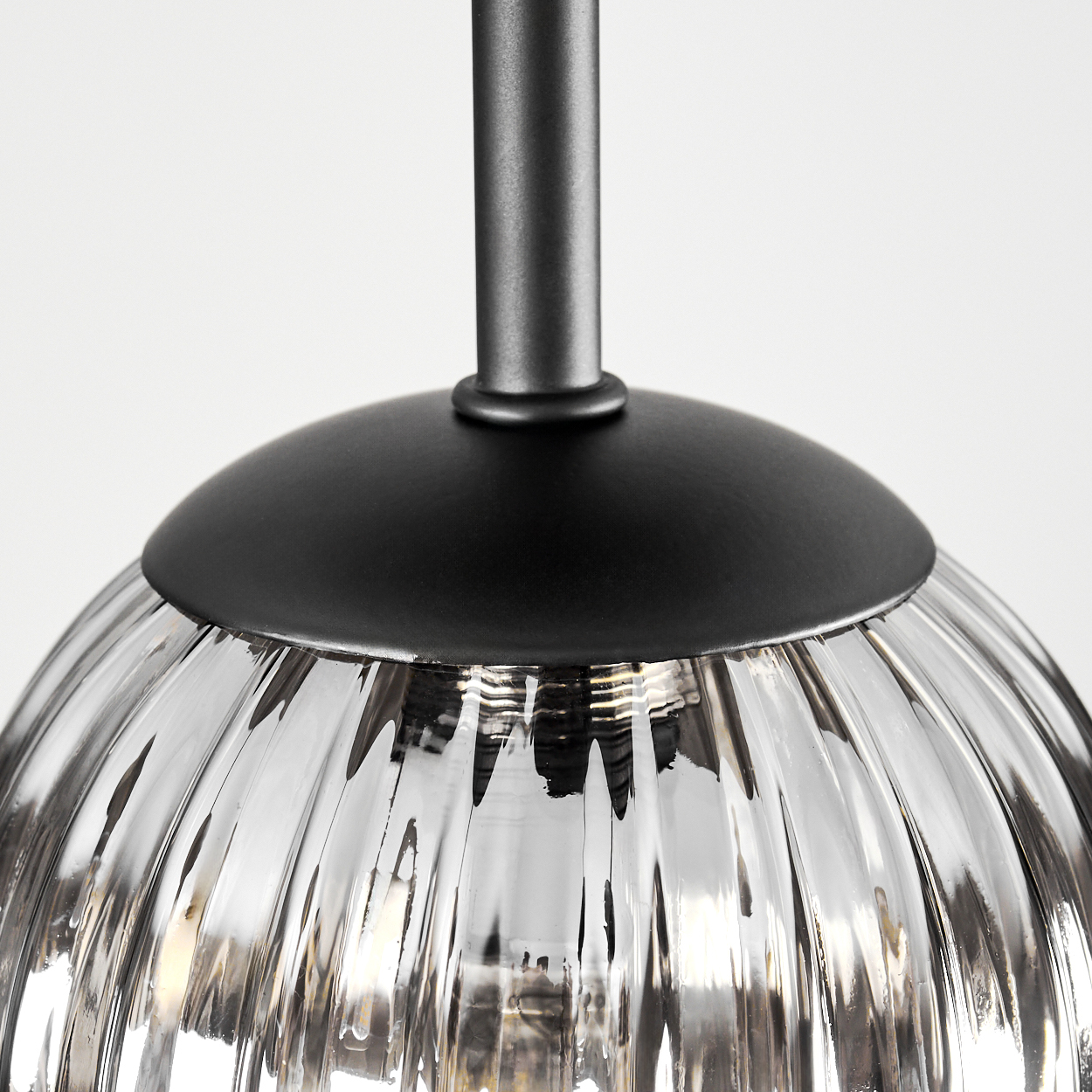 Nahaufnahme einer Glas-Pendelleuchte mit schwarzem Metallaufsatz und -schaft. Der Glasschirm ist gerippt und klar.