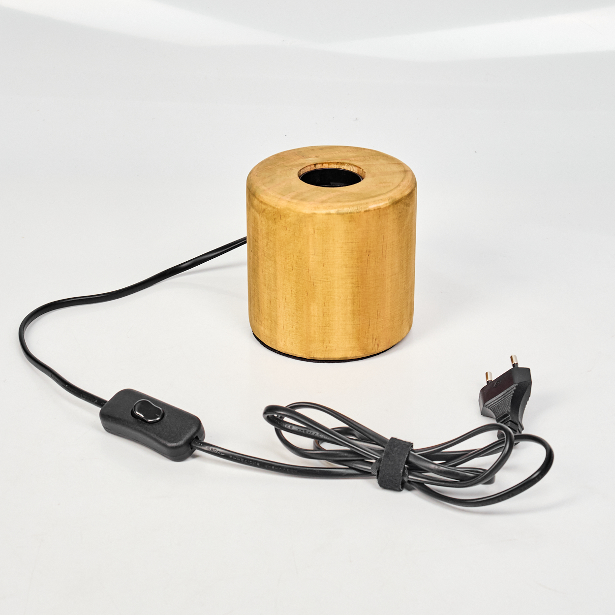 Eine zylindrische Holzlampe mit schwarzem Netzkabel, Schalter und Stecker. Die Lampe hat oben ein Loch.