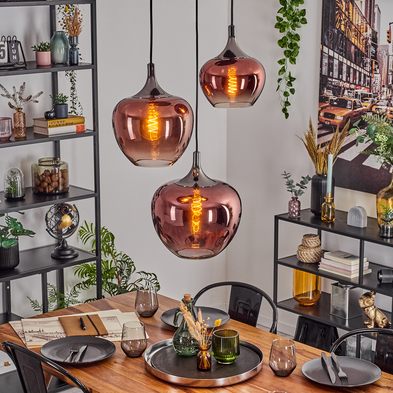 Esszimmer mit drei Hängelampen. Holztisch mit Tellern, Gläsern und Dekorationen. Regale mit Dekor im Hintergrund.