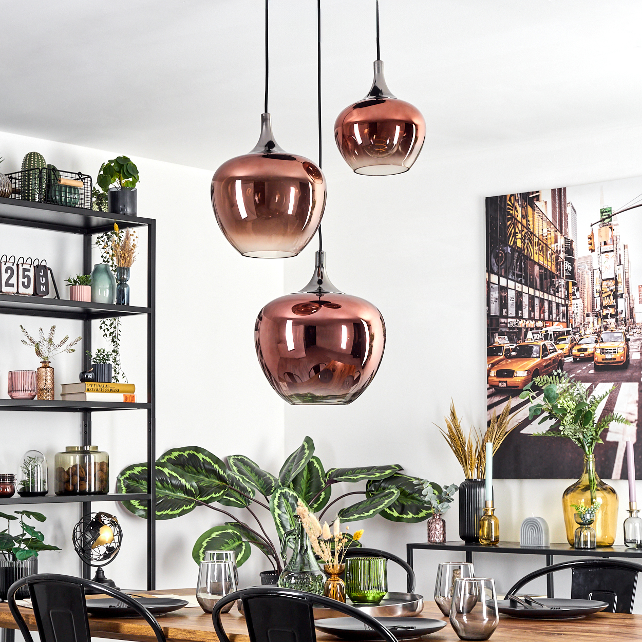 Esszimmer mit kupferfarbenen Pendelleuchten, Tisch und schwarzem Metallregal mit Pflanzen und Dekorationen.