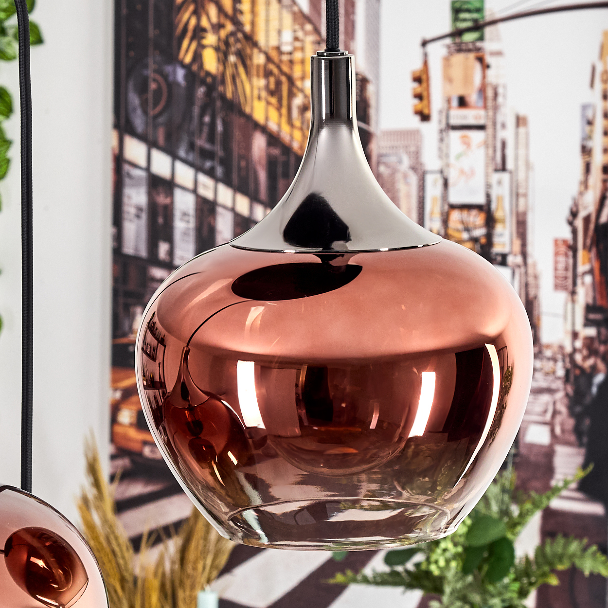 Eine kupferfarbene Pendelleuchte hängt. Die bauchige Form der Lampe spiegelt eine Straßenszene mit Stadtkulisse wider.
