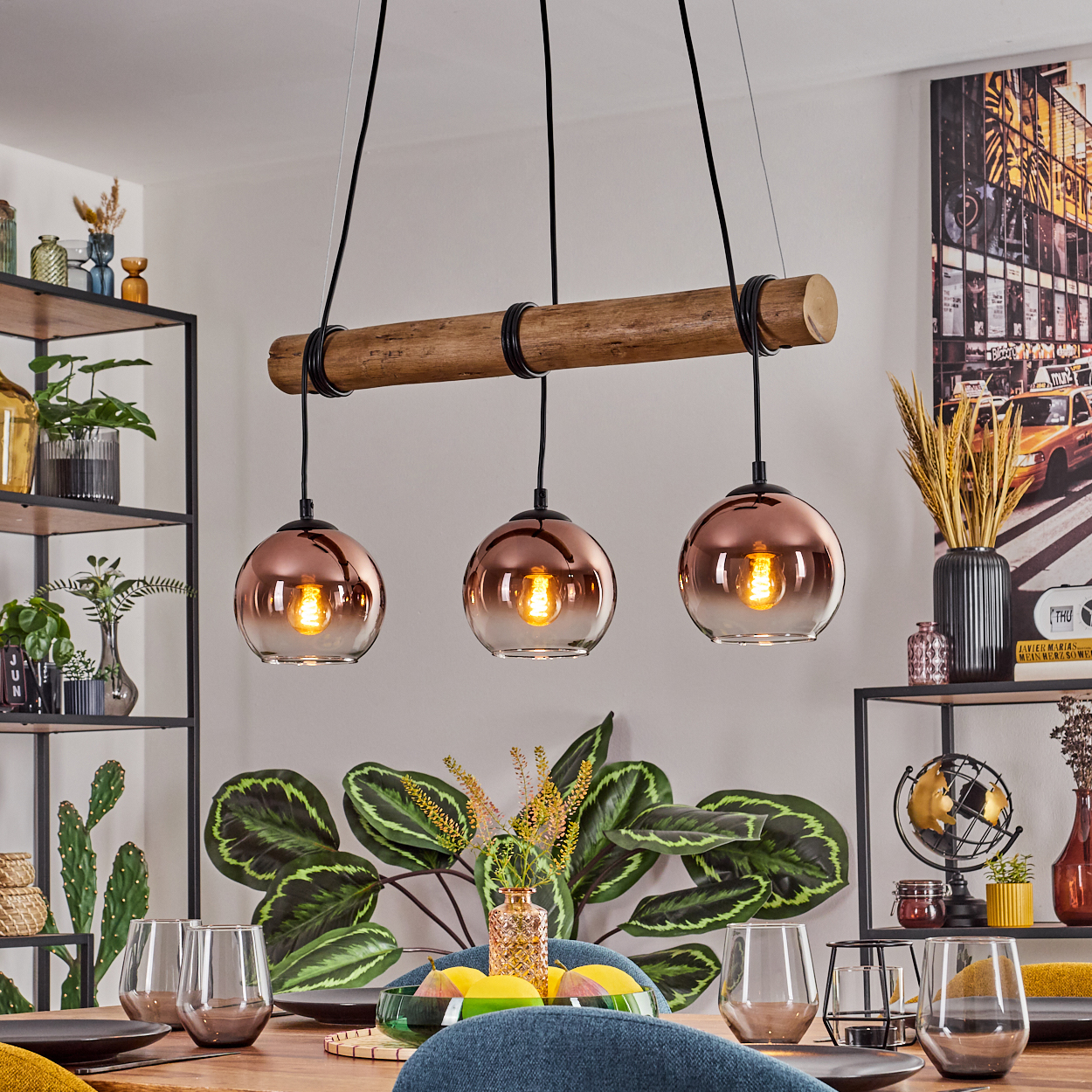 Esszimmer mit Holztisch, Kupfer-Pendelleuchten, Pflanzen und Gläsern. Ein Kunstwerk mit Stadtszene an der Wand.