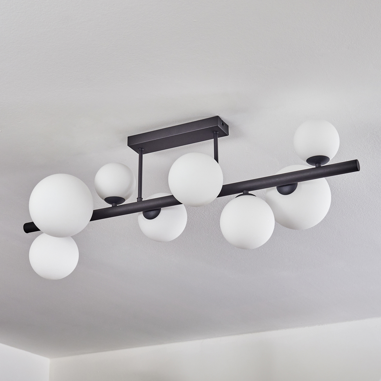 Eine moderne Deckenleuchte mit schwarzem Rahmen und mehreren weißen kugelförmigen Lichtern ist an einer weißen Decke befestigt.