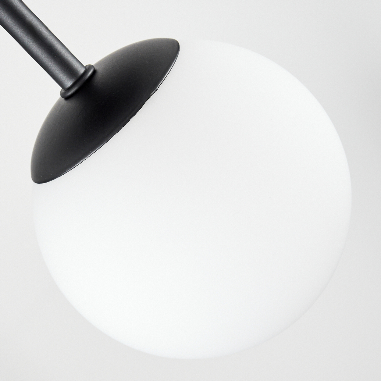Nahaufnahme einer modernen Lampe. Sie hat einen weißen, kugelförmigen Schirm mit einem schwarzen, gebogenen Arm.