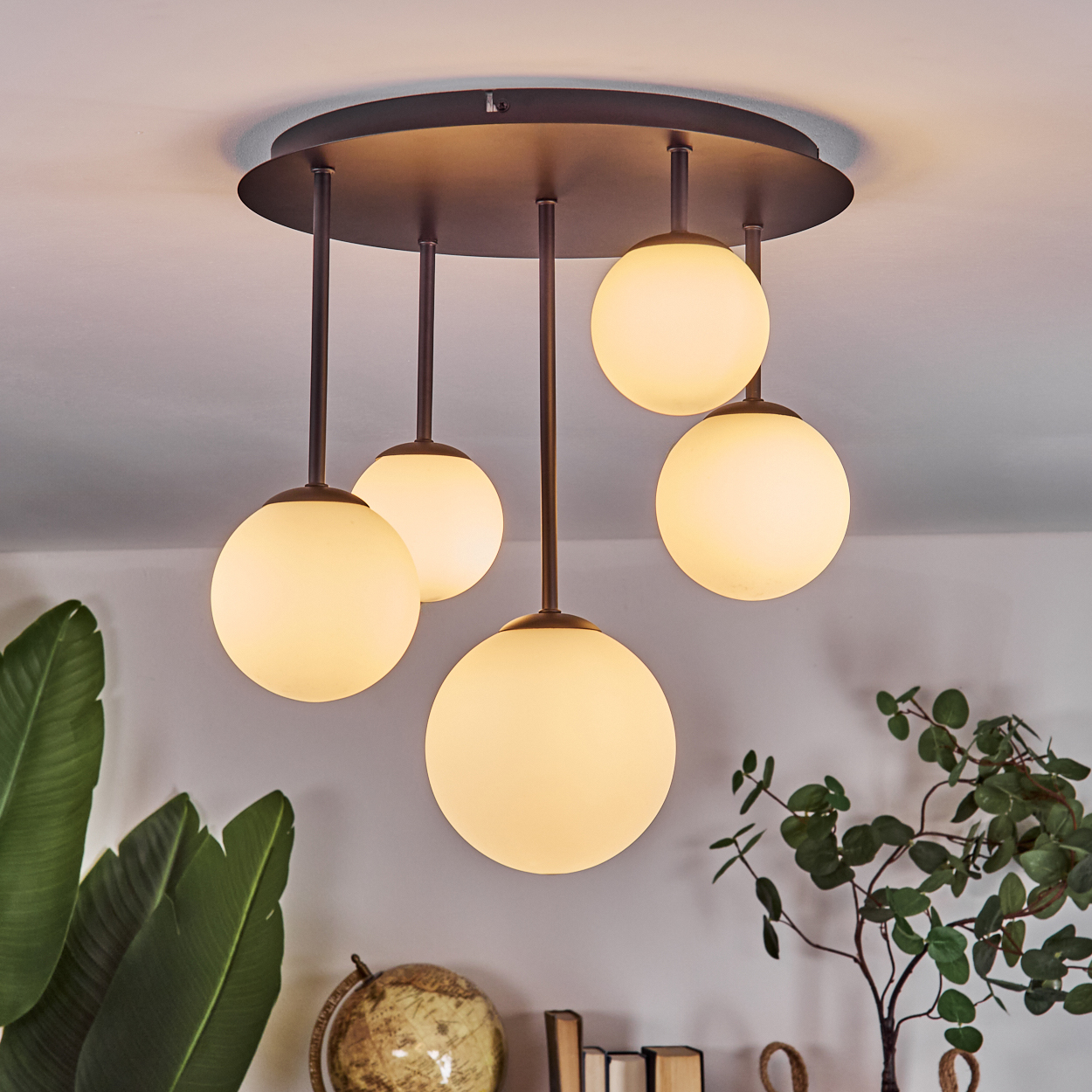 Moderne Deckenleuchte mit fünf kugelförmigen Lampen. Unten sind Globus und Pflanzen zu sehen. Das Licht ist an und beleuchtet den Raum.