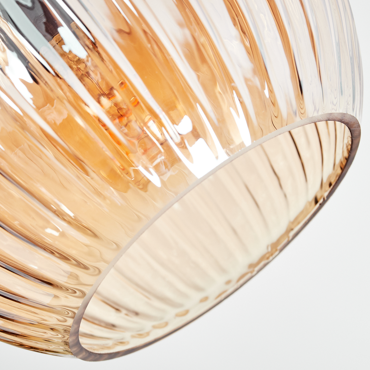 Nahaufnahme eines Glasschirms. Er ist bernsteinfarben, gerippt und teilweise durchsichtig. Im Inneren ist eine Glühbirne zu sehen.