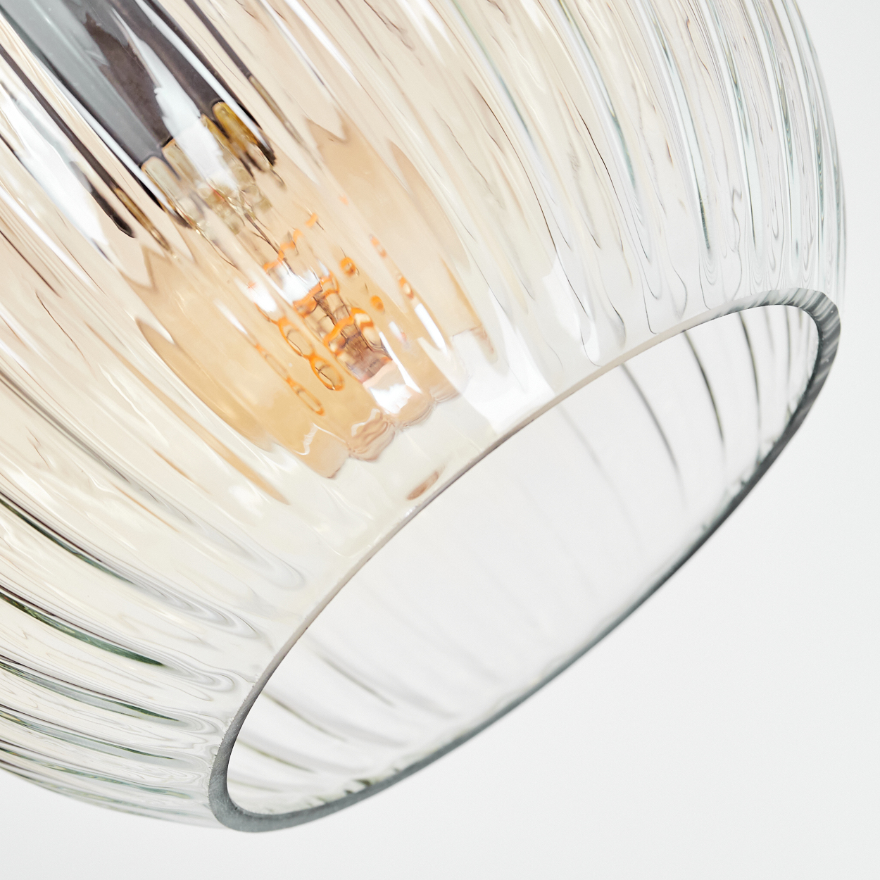 Nahaufnahme eines Lampenschirms aus Glas mit vertikalen Rippen. Im Inneren ist eine freiliegende Glühbirne zu sehen, vor weißem Hintergrund.