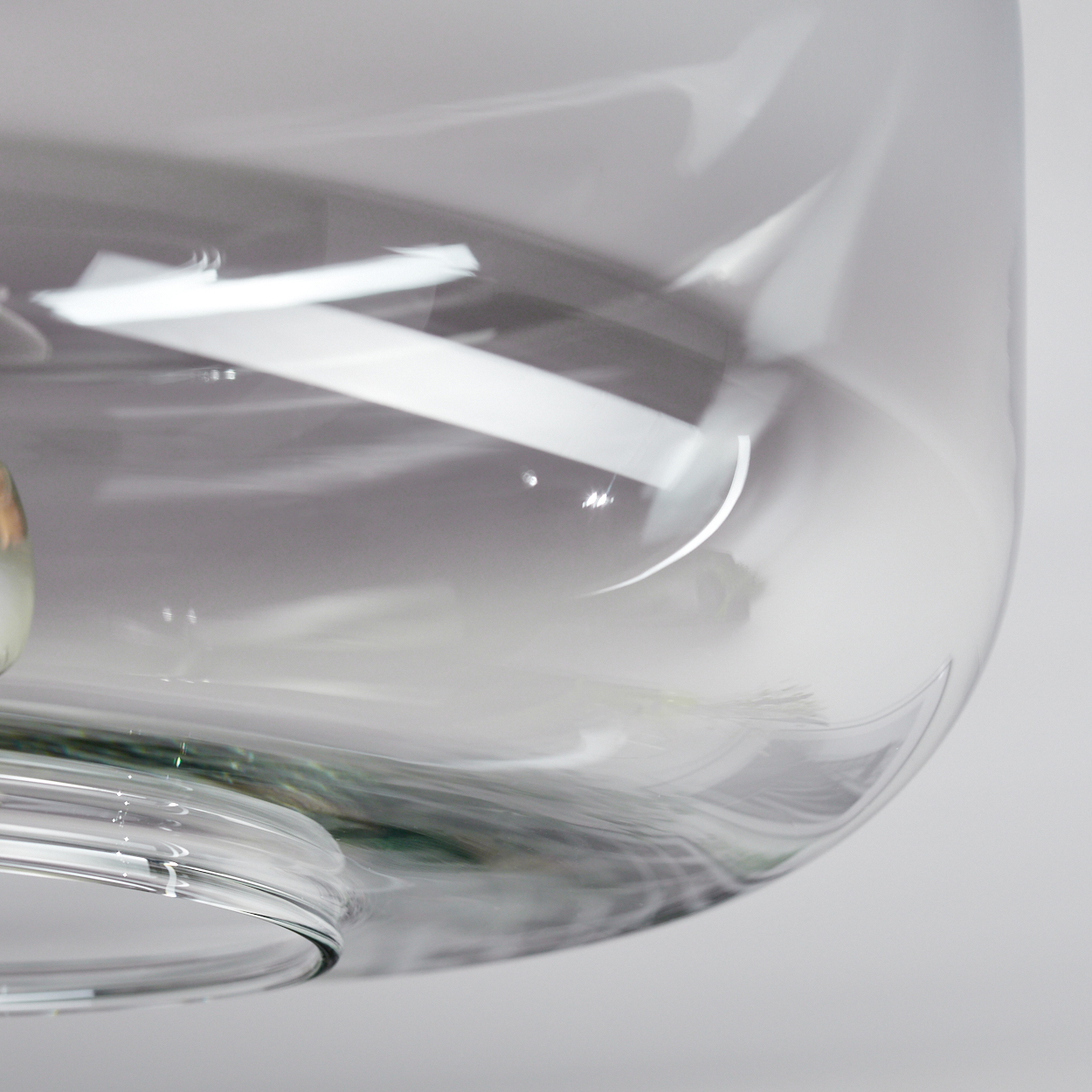 Nahaufnahme eines transparenten Glasobjekts mit abgerundeter Form. Reflexionen und Licht spielen auf der Oberfläche.