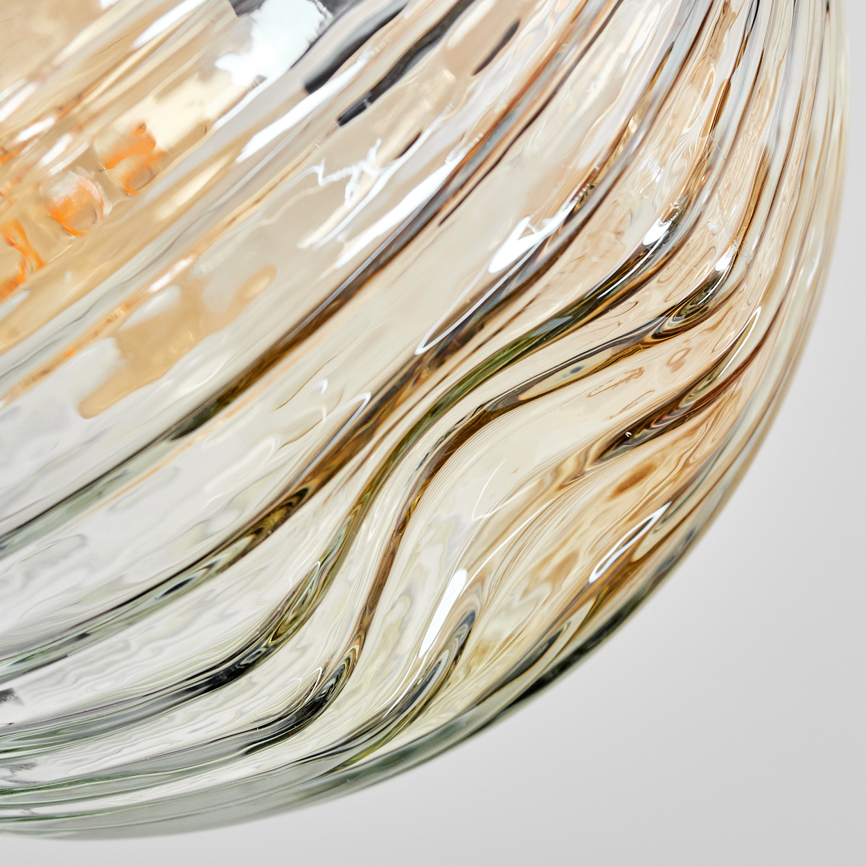 Nahaufnahme eines Glasobjekts mit wellenförmigem Muster. Das Glas hat bernsteinfarbene und klare Töne, wobei sich Licht auf der Oberfläche spiegelt.