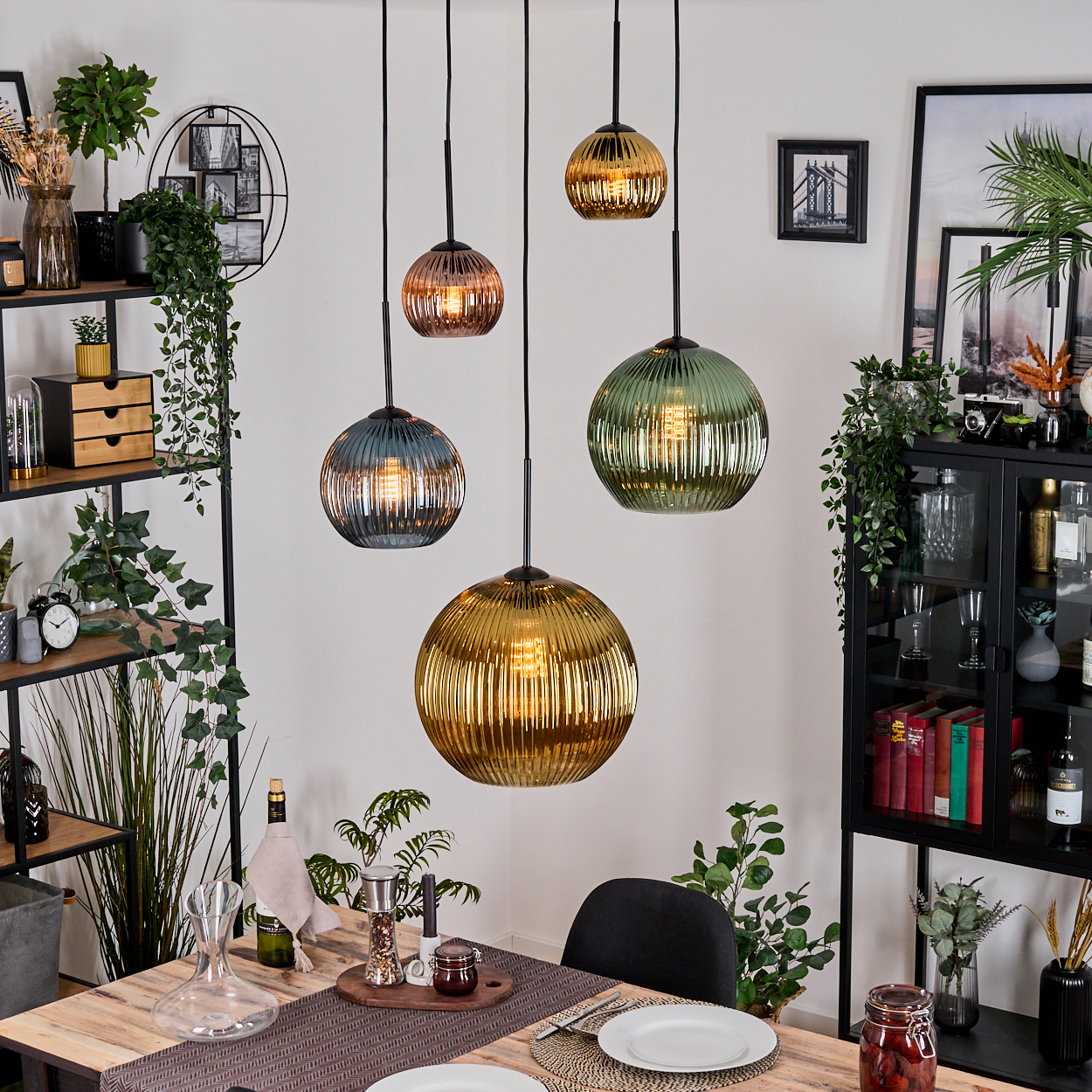 Esszimmer mit Hängekugelleuchten, Tisch mit Tellern und einer Vitrine mit Dekoration.