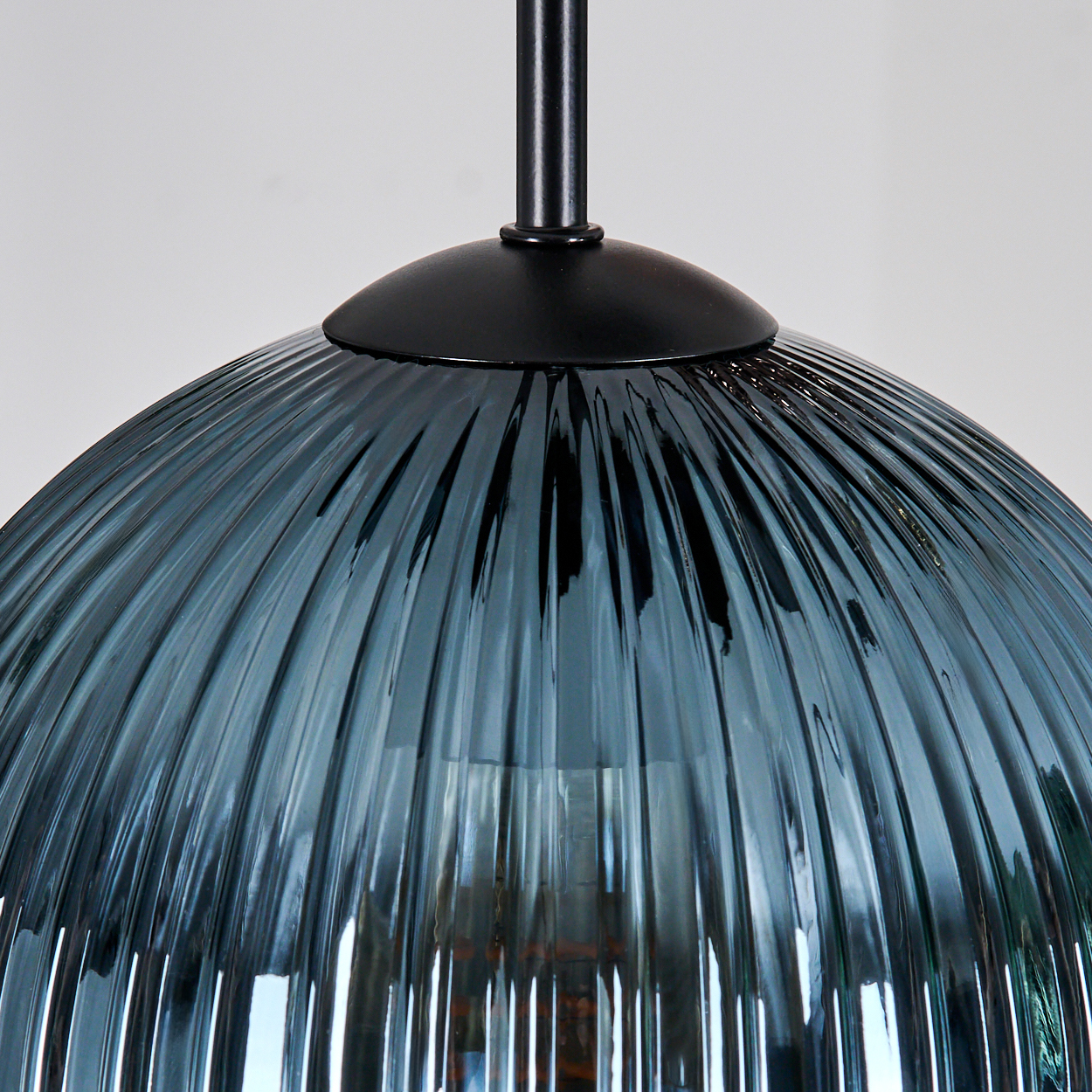 Nahaufnahme einer blauen Glas-Pendelleuchte. Die Lampe hat eine geriffelte Oberfläche und hängt an einer schwarzen Metallstange.