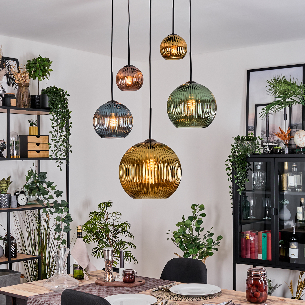 Esszimmer mit hängenden Kugelleuchten. Tisch mit Tellern. Regale und Schrank mit Pflanzen und Dekoration.