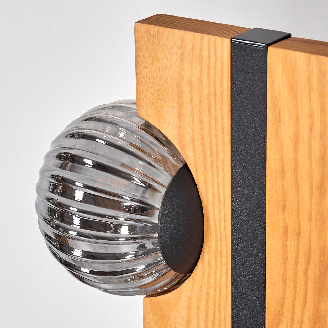 Eine dekorative Lampe mit geripptem Glaskugel, gehalten von einer Holzstruktur mit einem schwarzen Metallband, vor weißem Hintergrund.