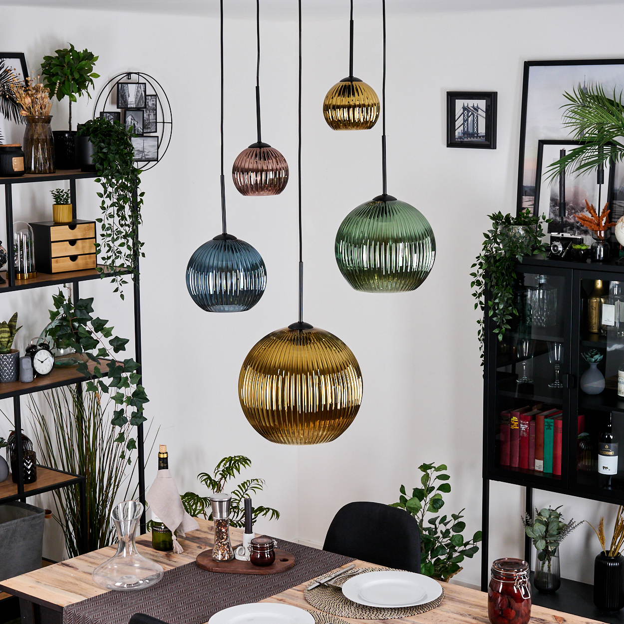 Esszimmer mit mehreren Hängelampen in verschiedenen Farben. Ein Holztisch mit Tellern und einem schwarzen Stuhl. Regale und Dekorationen an den Seiten.