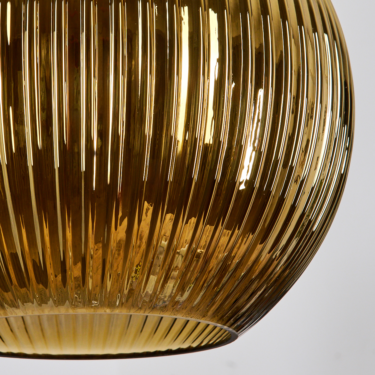 Nahaufnahme eines goldenen, gerippten Glasschirmes. Licht reflektiert von der Oberfläche. Der Hintergrund ist weiss.