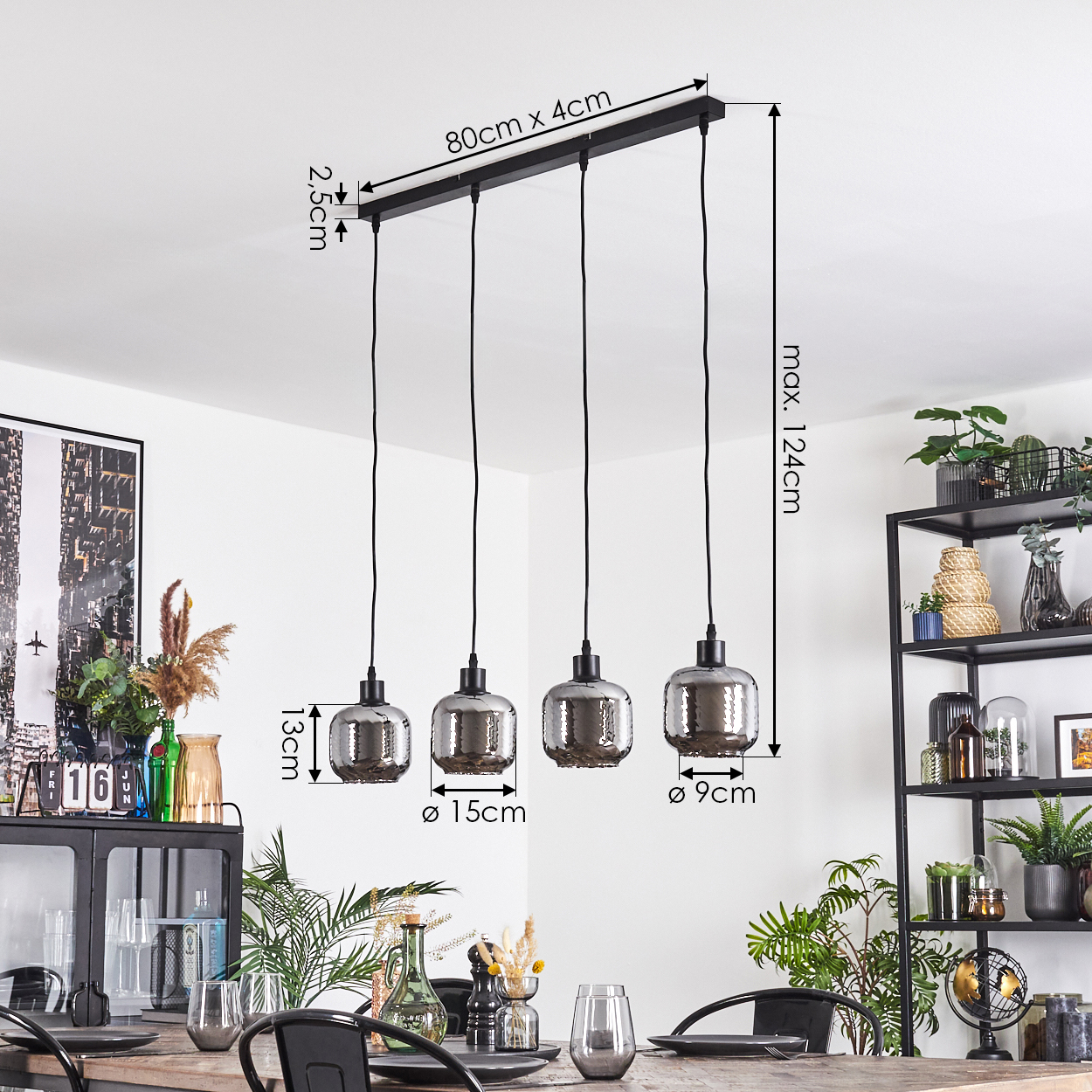 Ein Esszimmer mit einem schwarzen Metallkronleuchter mit vier Rauchglaslampen. Maße sind angegeben. Pflanzen und Möbel sind sichtbar.