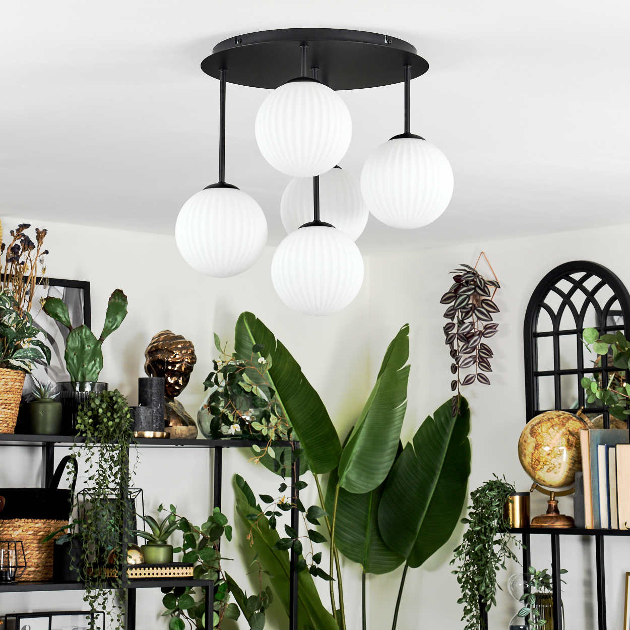 Ein modernes Interieur mit einer schwarzen Deckenlampe mit weißen Kugeln, Pflanzen und Regalen mit Dekorationsartikeln.