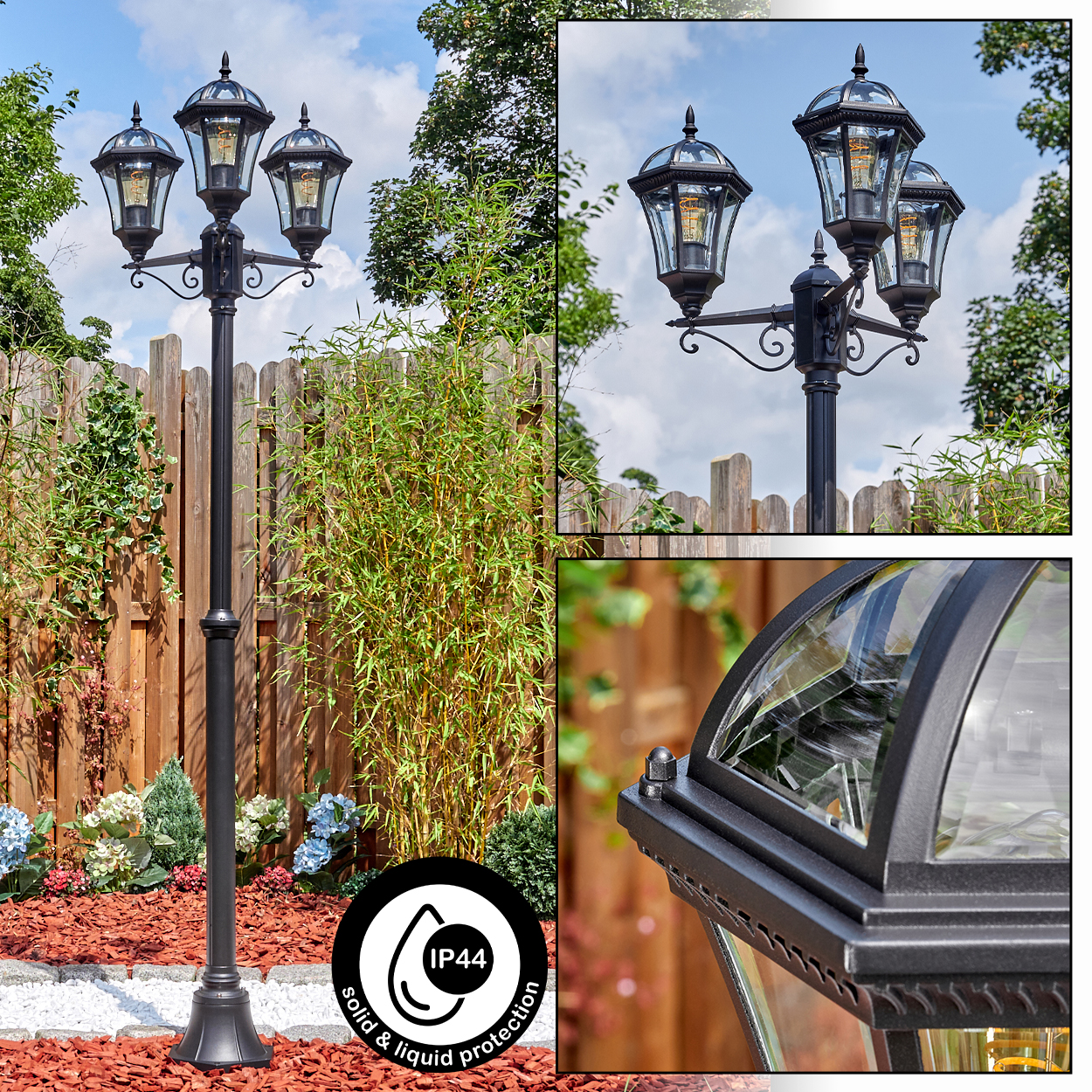 Schwarze Außenlampe mit drei Lichtern. Dahinter ein Holzzaun, grüne Pflanzen und ein blauer Himmel.