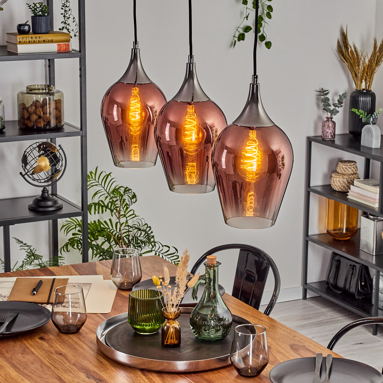 Esszimmer mit drei Hängelampen. Tisch mit Gläsern und Tellern gedeckt. Regale mit Deko sind im Hintergrund.