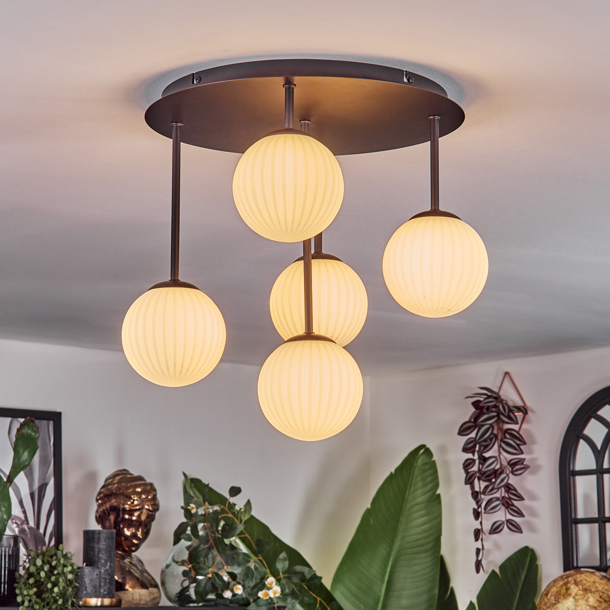 Moderne Deckenleuchte mit fünf kugelförmigen Lampen. Die Lampen sind cremefarben und hängen von einem dunklen Metallsockel ab.