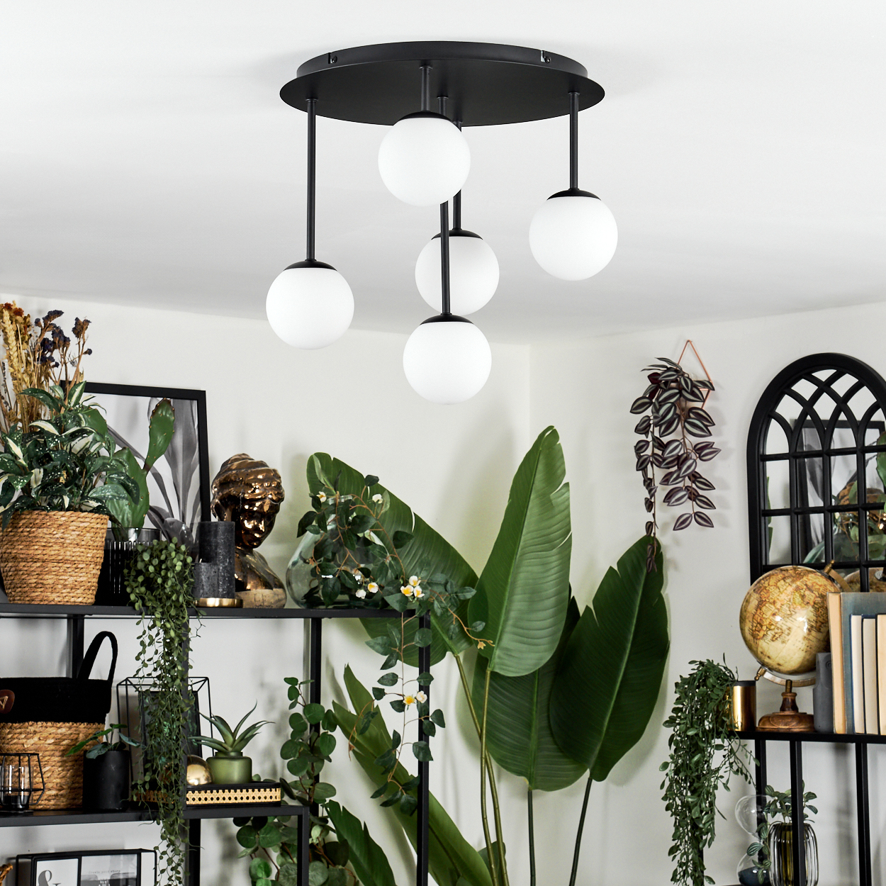Ein modernes Zimmer mit einer schwarz-weißen Leuchte, Regalen mit Pflanzen, einem Globus und einem Spiegel.