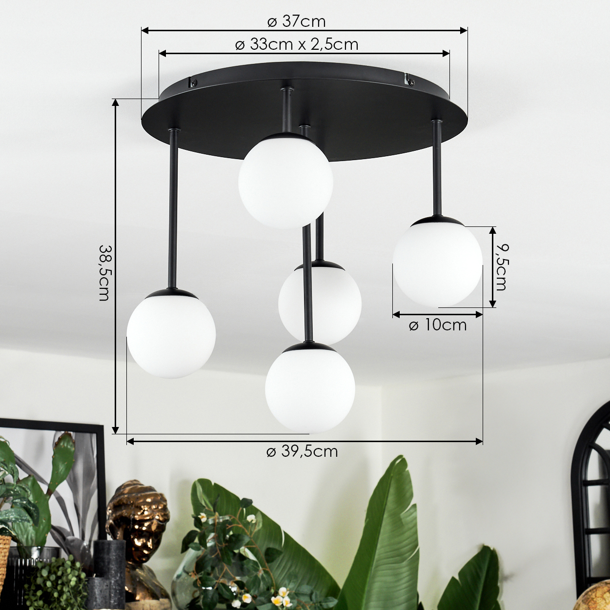 Eine moderne Deckenlampe mit fünf weißen Glaskugelschirmen. Die Lampe hat einen schwarzen Sockel und schwarze Stäbe. Pflanzen und eine Statue im Vordergrund.