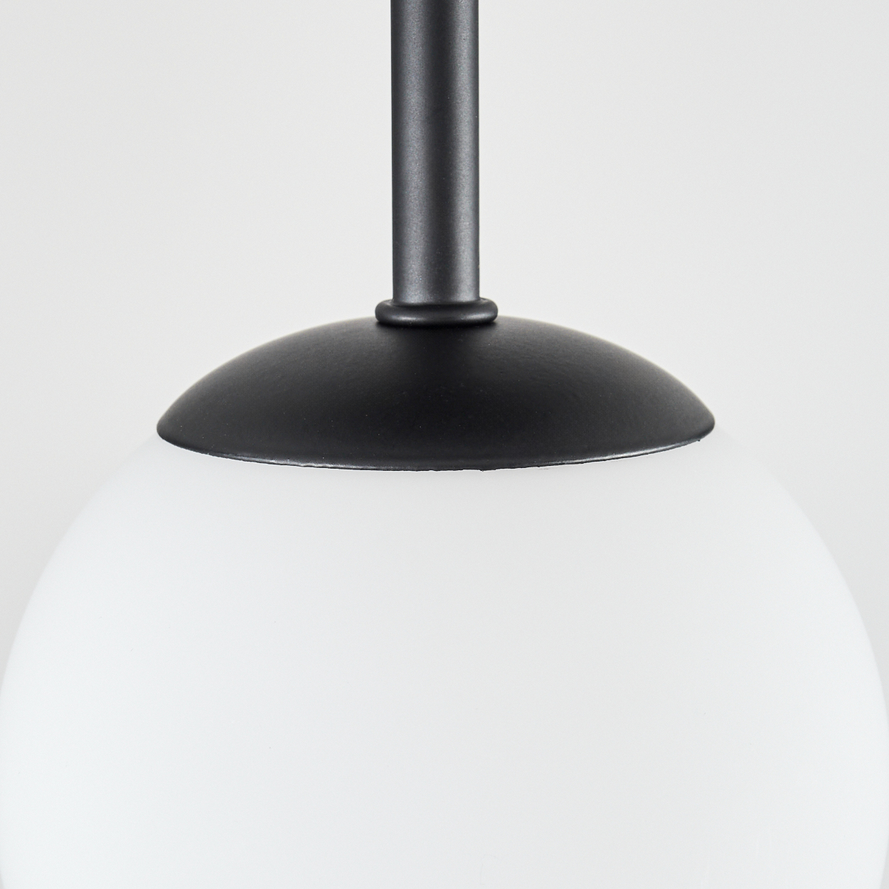 Nahaufnahme einer schwarz-weißen Pendelleuchte. Die Lampe hat einen schwarzen Stiel und Schirm, mit einer weißen, runden Glühbirne.