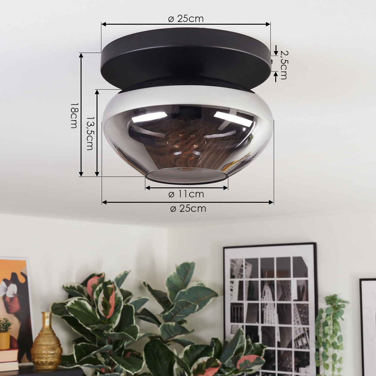 Eine moderne Deckenlampe mit schwarzen und silbernen Farbtönen ist installiert. Abmessungen sind angegeben. Pflanzen, Rahmen und eine goldene Vase sind im Hintergrund.