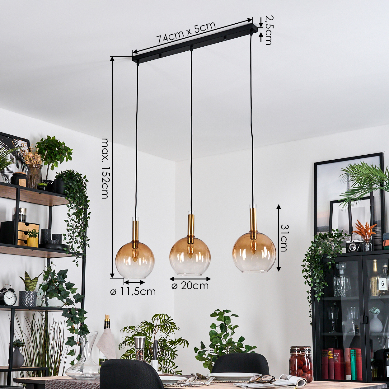 Drei Pendelleuchten mit orangefarbenen Glasschirmen hängen an einer schwarzen Halterung. Abmessungen sind angegeben. Pflanzen und Möbel im Hintergrund.