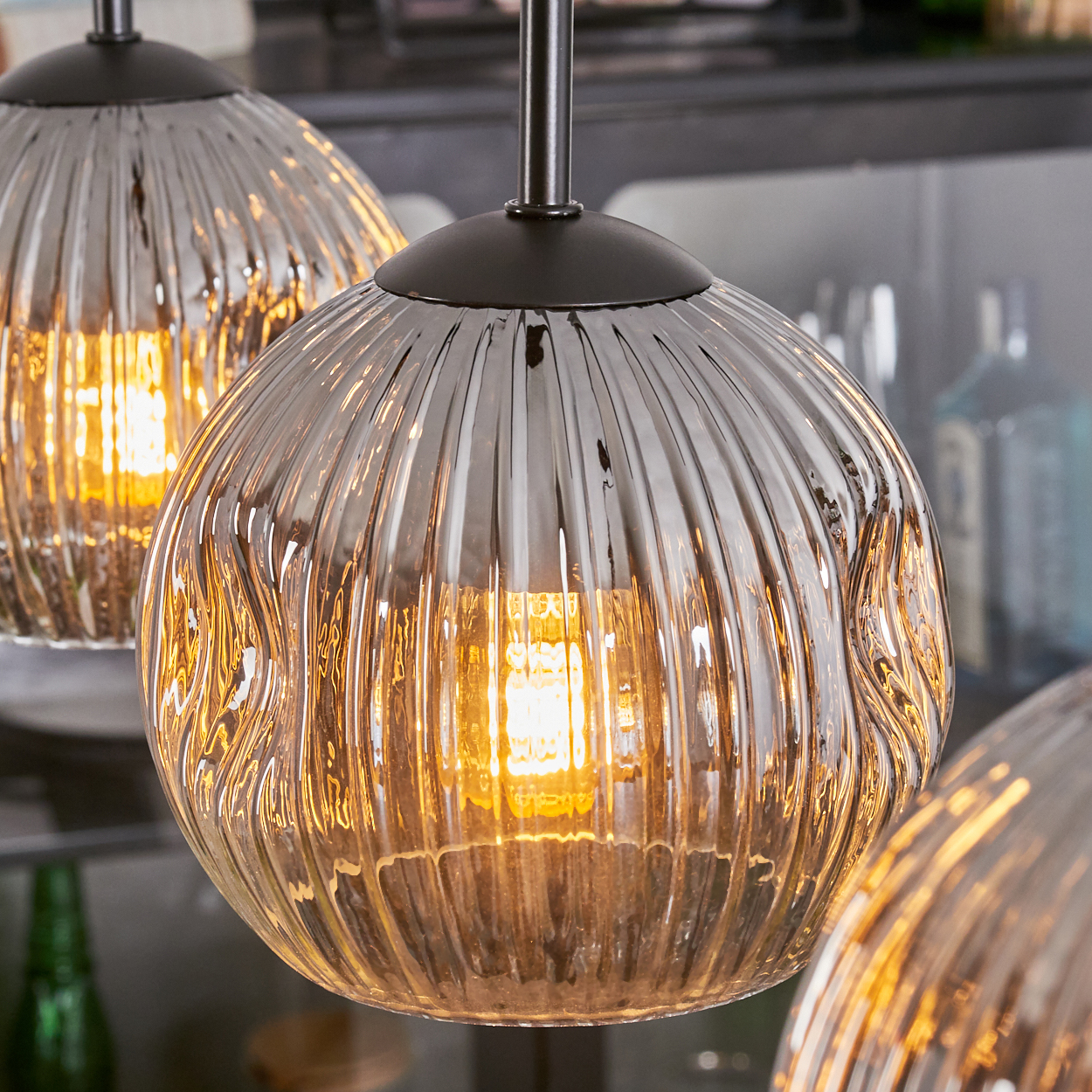 Nahaufnahme von drei Glaskugelleuchten mit strukturierter Oberfläche, die warmes Licht aussenden. Dunkle Metallstiele und -armaturen sind sichtbar.