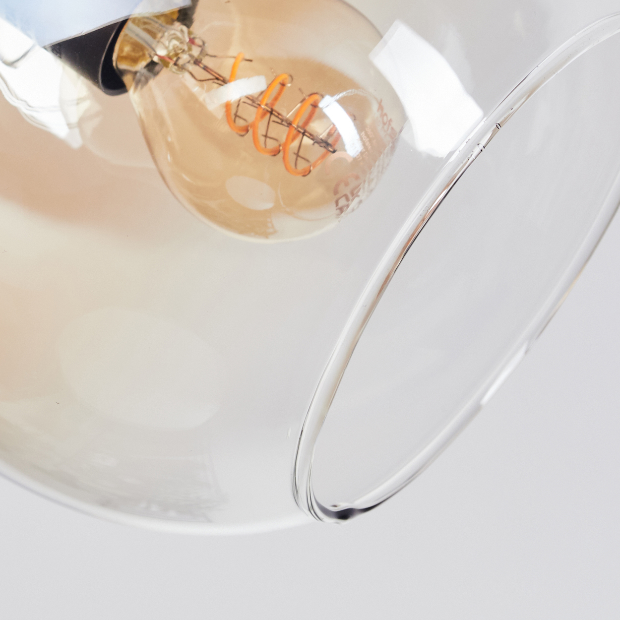Nahaufnahme einer Leuchte mit Glasschirm und Glühbirne mit orangem Glühfaden.