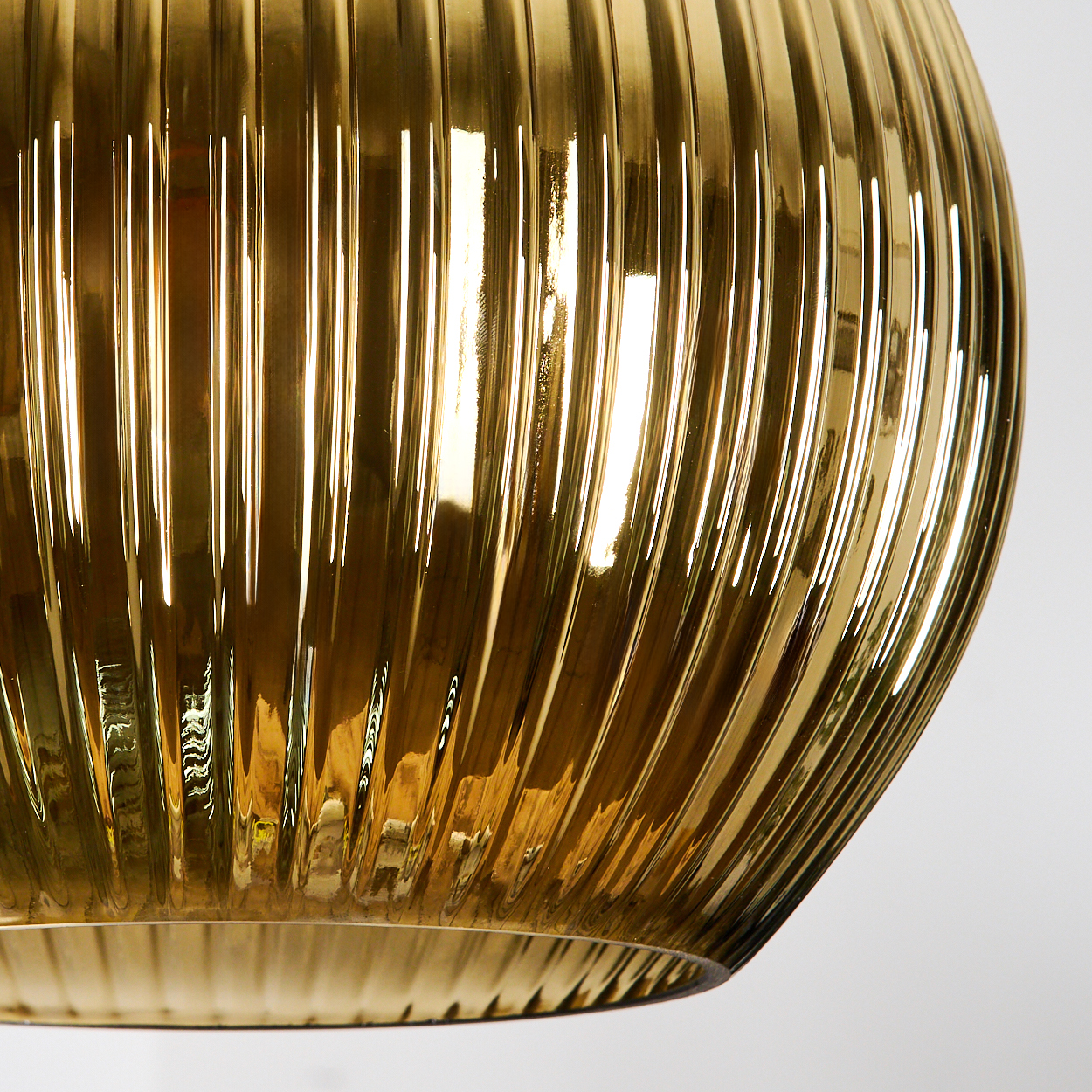 Nahaufnahme eines goldenen Glasobjekts mit vertikalen Rippen. Der Hintergrund ist weiß. Licht reflektiert sich im Glas.
