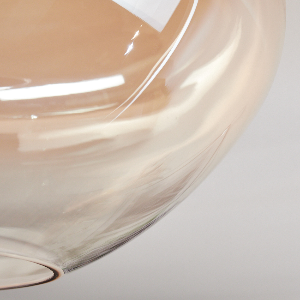 Nahaufnahme eines Glasobjekts mit hellbraunem Farbton. Das Glas ist gebogen und hat Reflexionen. Der Hintergrund ist weiß.