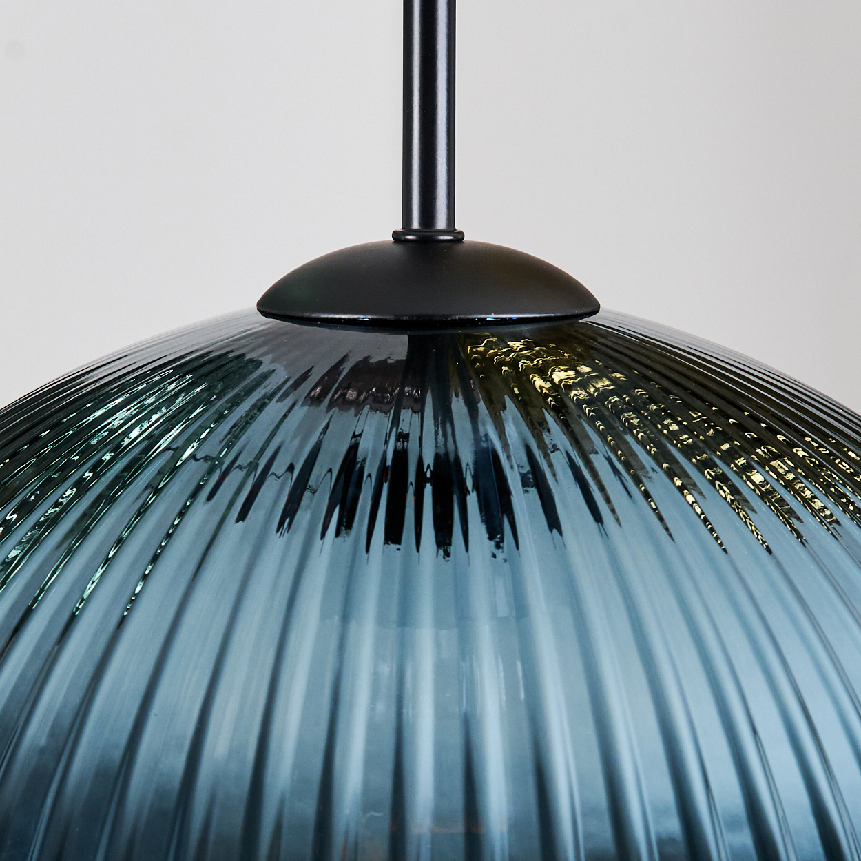 Nahaufnahme eines Glasschirms mit Rippendesign. Er ist tealfarben und hat einen schwarzen Metallschaft und eine Montageplatte.