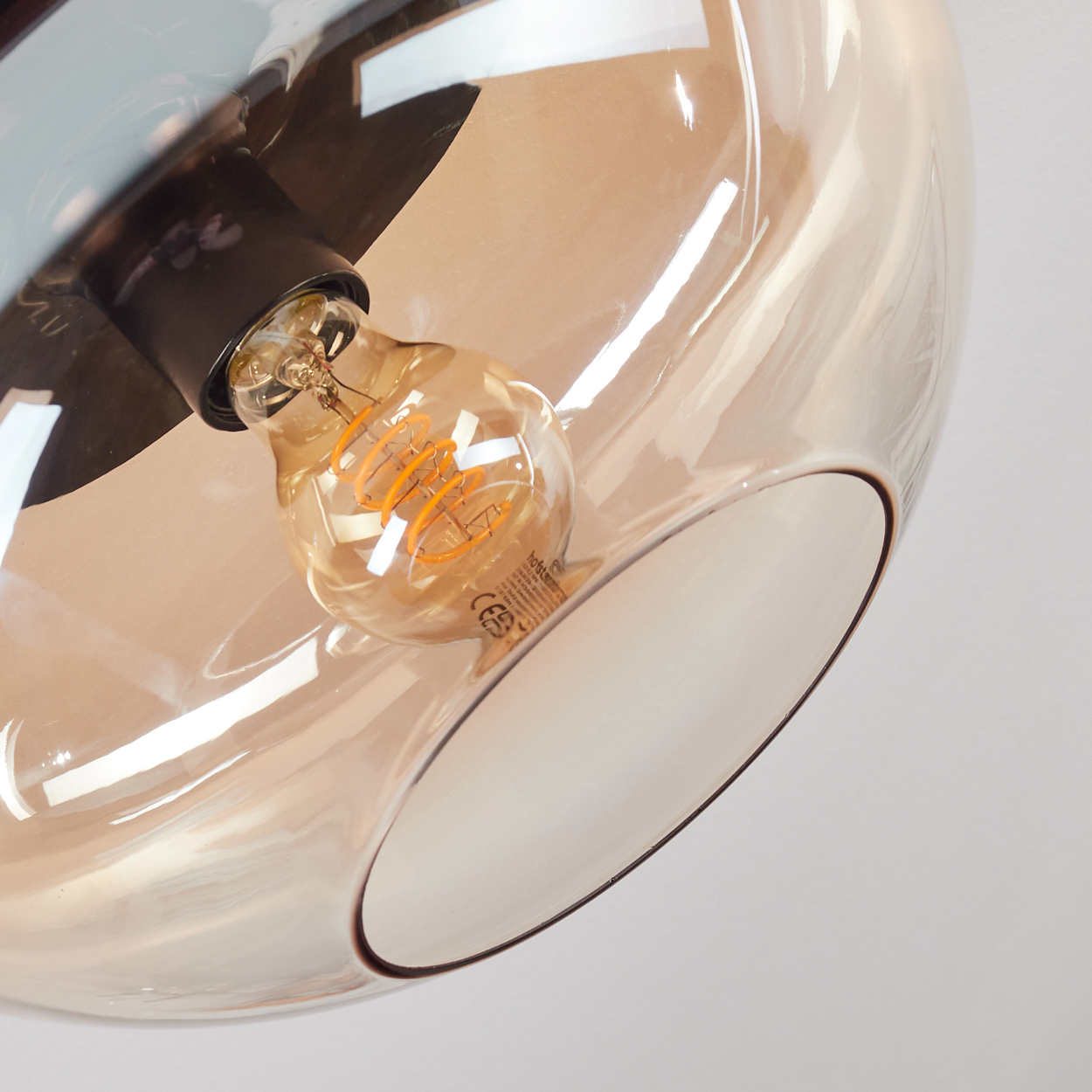 Nahaufnahme einer Leuchte mit braunem Glasschirm und sichtbarer Glühbirne. Die Glühbirne leuchtet warm.