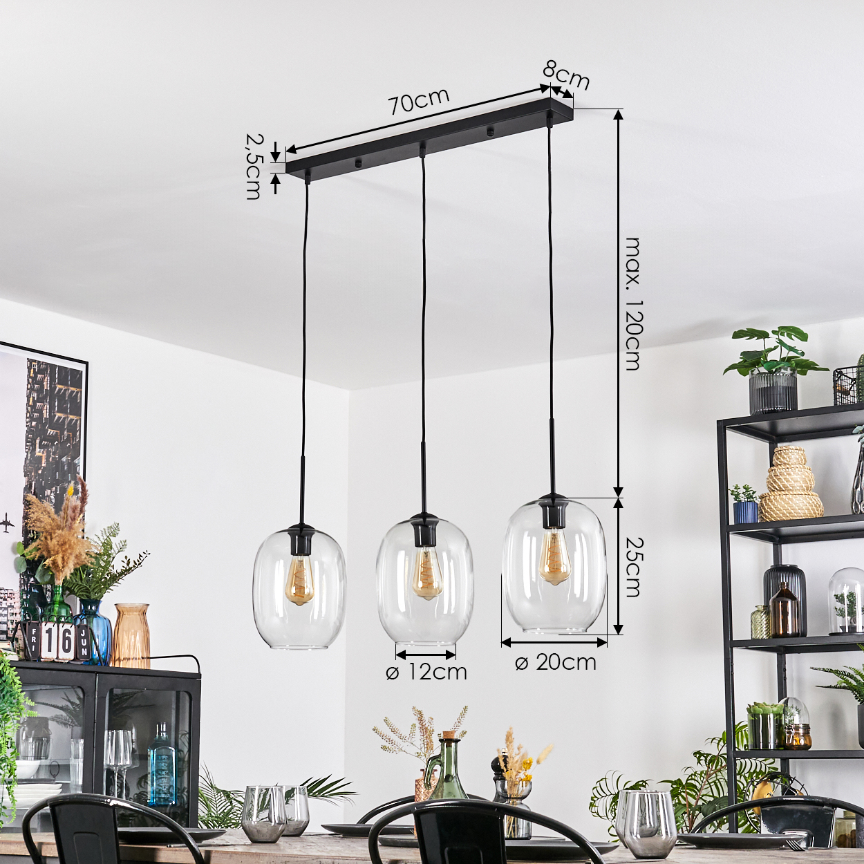 Drei Glas-Pendelleuchten mit sichtbaren Glühbirnen hängen über einem Esstisch. Abmessungen sind angegeben. Hintergrund umfasst Deko und Regale.
