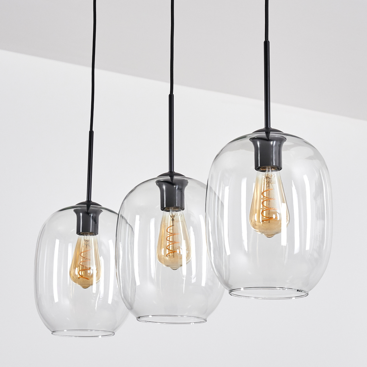 Drei Glas-Pendelleuchten mit schwarzer Hardware und freiliegenden Glühbirnen vor weißem Hintergrund.
