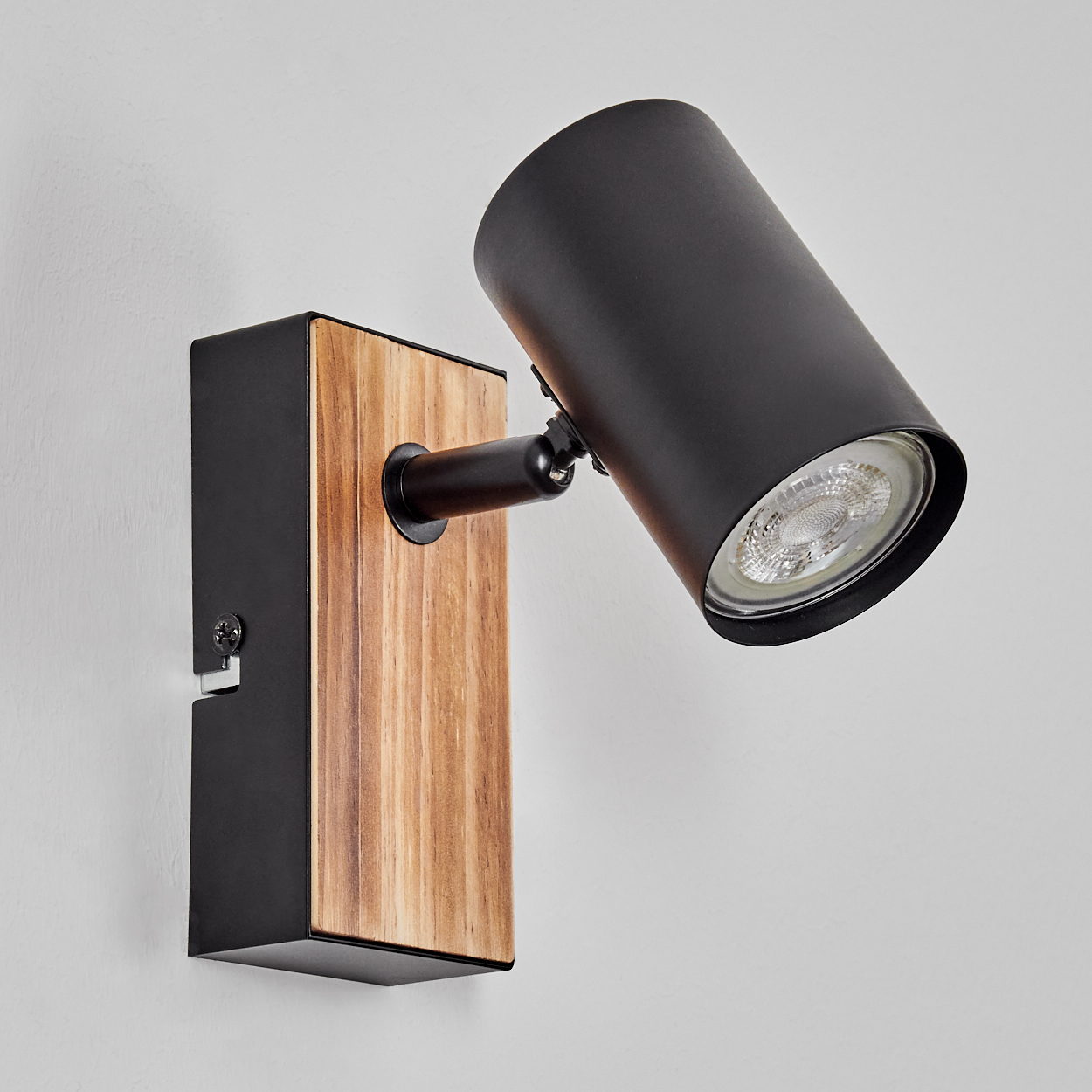 Eine moderne Wandleuchte mit schwarzem zylindrischen Kopf und Holzsockel, an einer weißen Wand montiert.