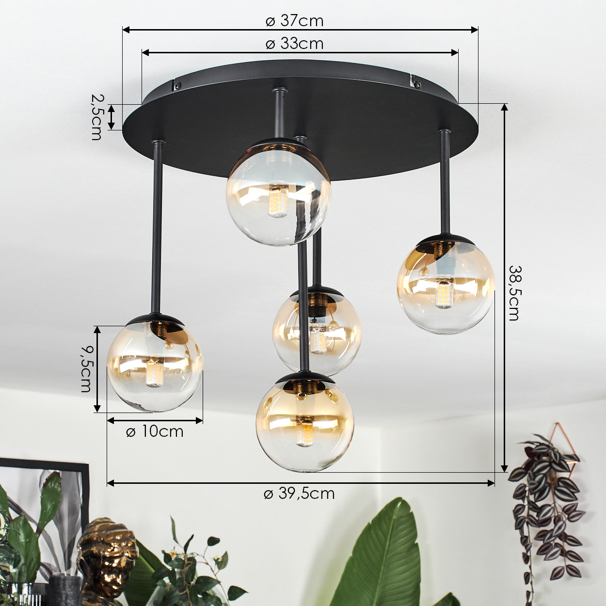 Moderne Deckenlampe mit fünf kugelförmigen Glasschirmen, schwarzem Rahmen und Maßen. Pflanzen sind im Hintergrund sichtbar.