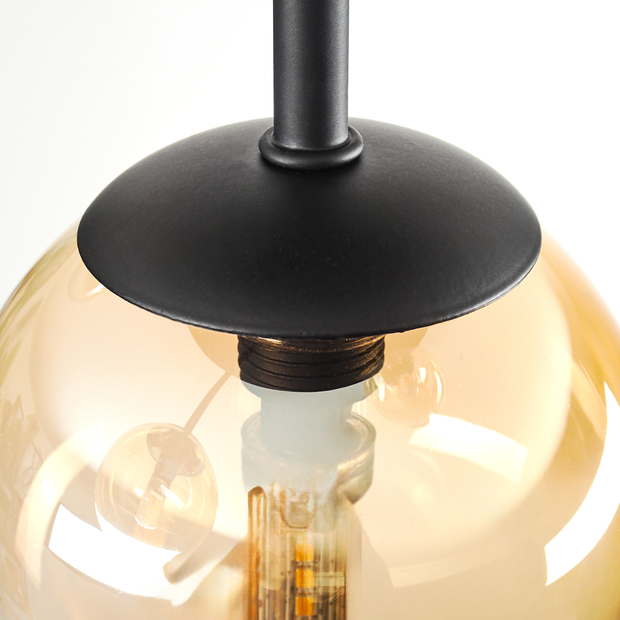 Nahaufnahme einer schwarzen Lampe mit einem kugelförmigen, bernsteinfarbenen Glasschirm. Die Glühbirne ist innen sichtbar.