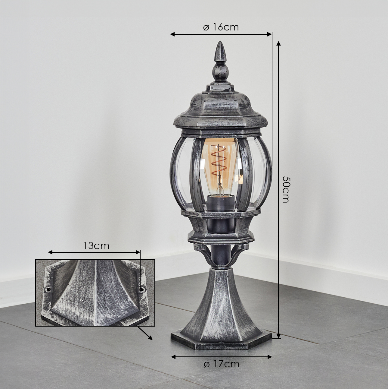 Eine dekorative Außenlampe, silbergrau, mit klaren Glasscheiben. Abmessungen sind angegeben. Eine detaillierte Ansicht einer Wandhalterung wird gezeigt.