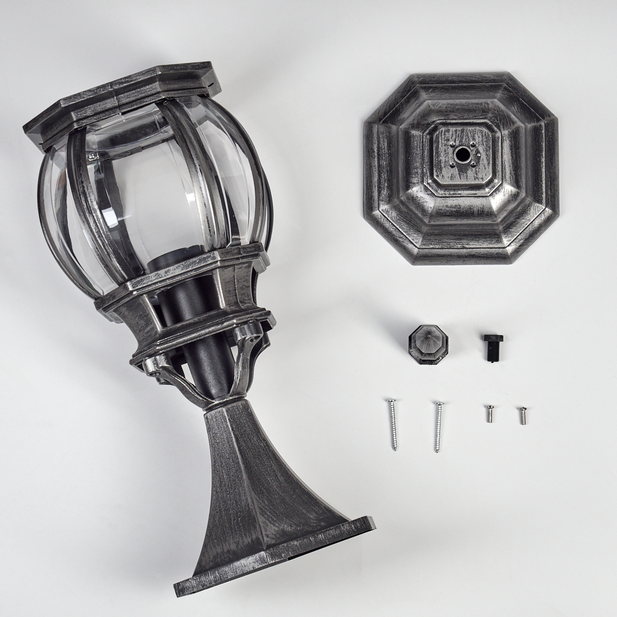 Eine zerlegte Außenlampe mit silbernem Finish, einschließlich Lampenkopf, Sockel, Schrauben und anderer Komponenten auf weißer Oberfläche.