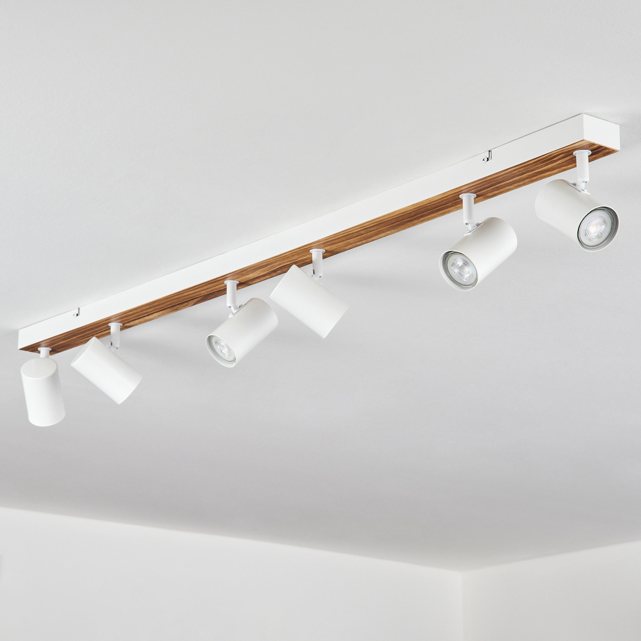 An der Decke montierte Leuchte. Weiße Strahler auf Holz- und Weißsockel. Der Hintergrund ist eine weiße Decke.