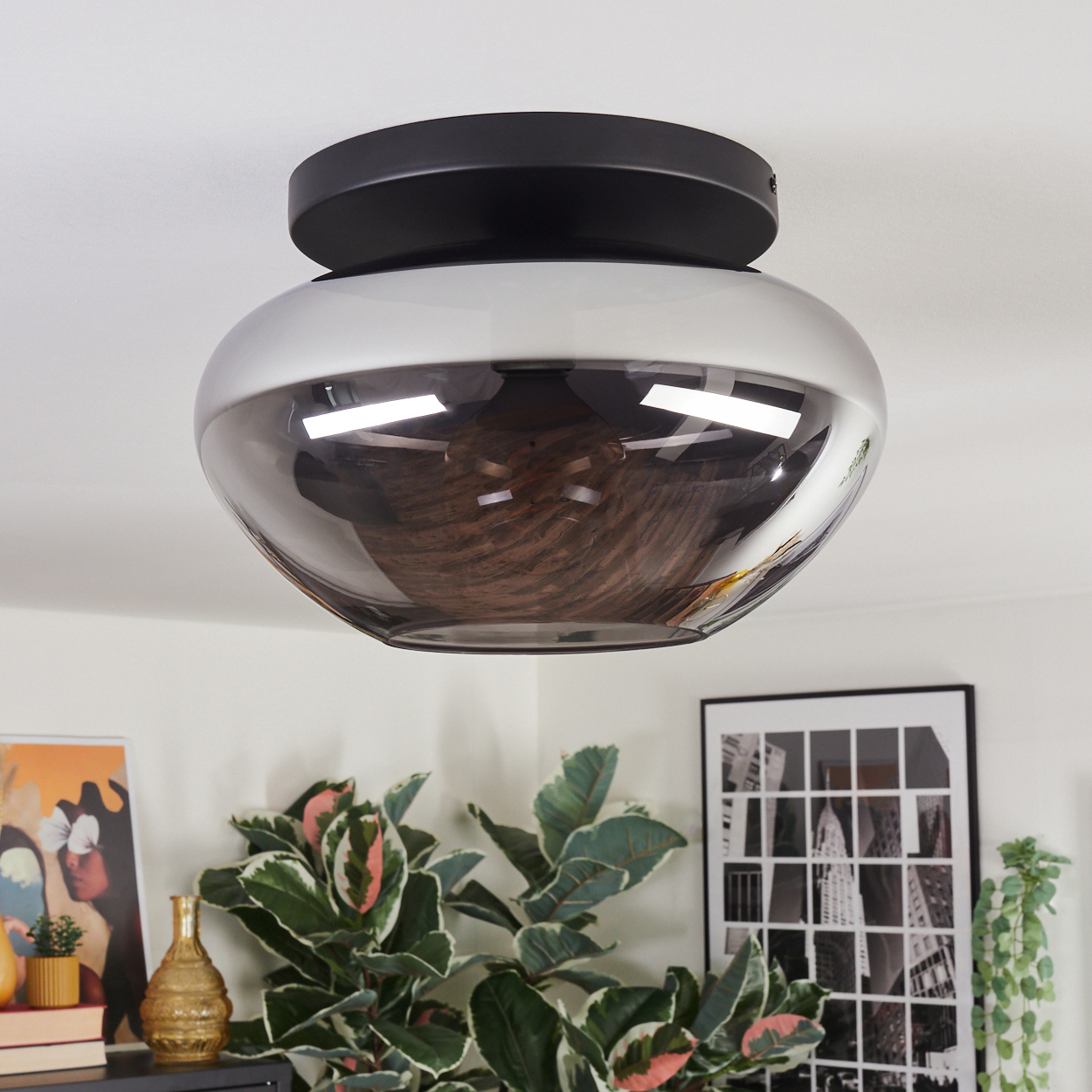 Eine moderne Deckenleuchte mit schwarzem Sockel und Rauchglasschirm. Der Raum hat Pflanzen, Kunst und ein schwarzes Regal.