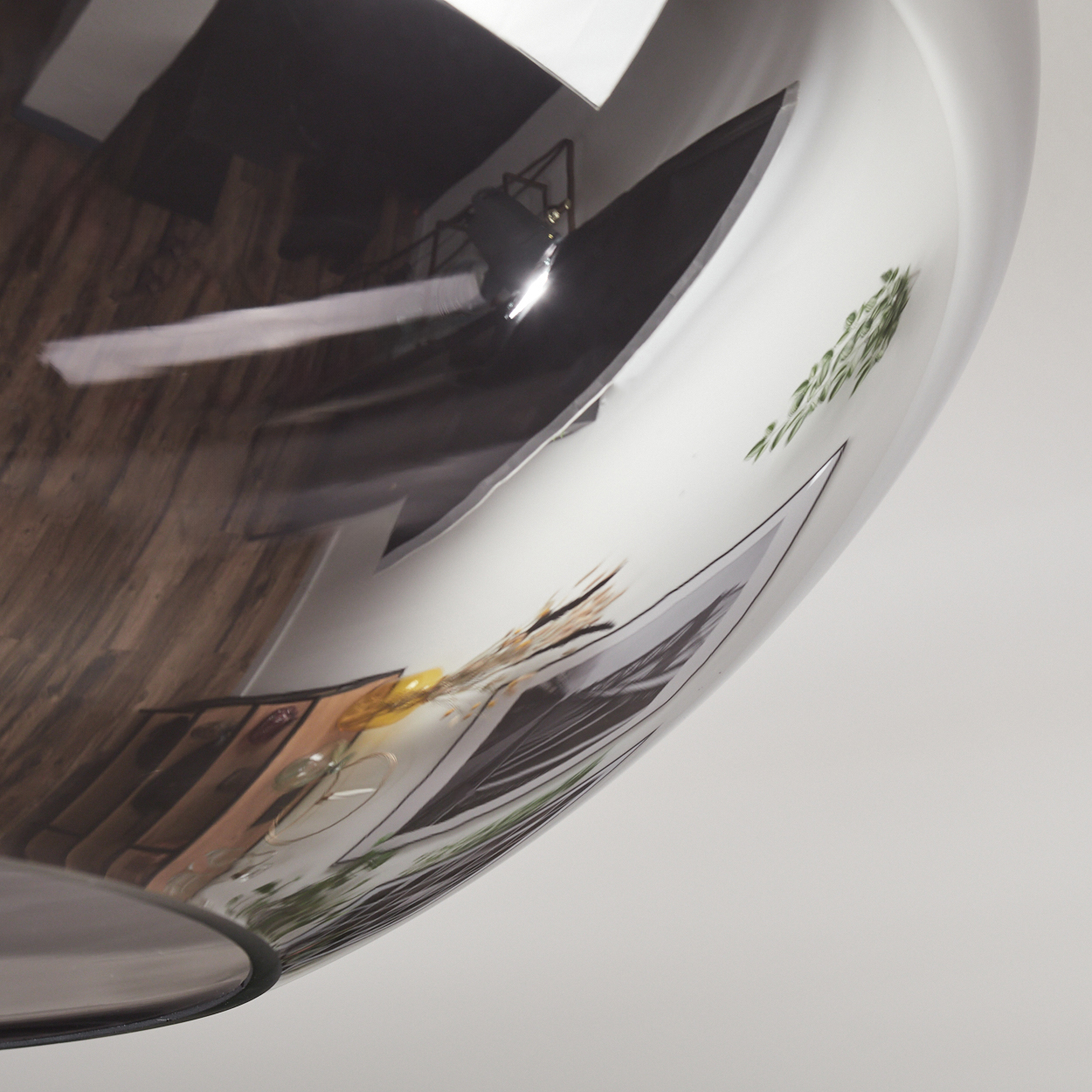 Eine reflektierende Oberfläche zeigt einen Holzboden, ein Licht und ein Schwarz-Weiß-Bild von Pflanzen und Essen, vor weißem Hintergrund.