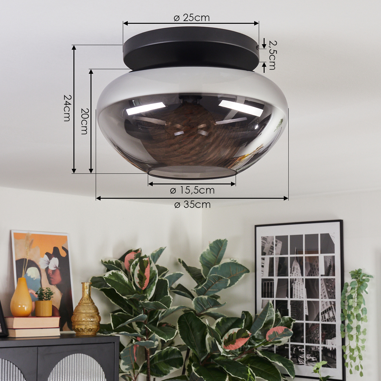Eine moderne Deckenlampe mit schwarzem Sockel und rauchfarbenem Glasschirm, Maße beschriftet. Darunter ein dekorierter Schrank mit Kunst und Pflanzen.