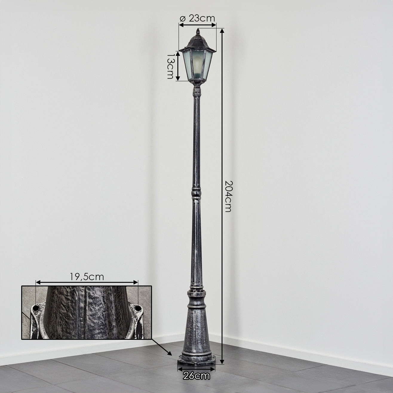 Eine dekorative, hohe, schwarze Straßenlaterne mit Maßangaben. Sie steht auf einem gefliesten Boden vor einer weißen Wand.